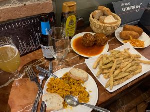 Dónde comer bien y barato en Granada: diferentes tapas en una mesa (paella, berenjenas rebozadas con miel, croquetas, albóndigas en salsa) y una cerveza sin alcohol.