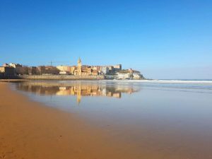 Qué hacer en Gijón: playa de San Lorenzo con la iglesia de San Pedro al fondo, reflejada en el mar en calma