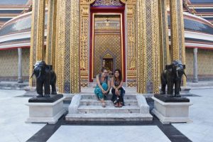 viaje a Tailandia: con Andrea sentadas en unas pequeñas escaleras a la entrada de un templo. Hay dos estatuas de elefantes a ambos lados.