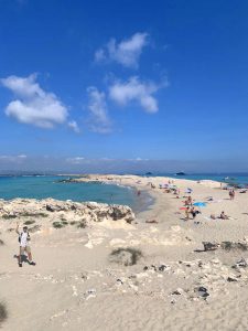 Qué hacer en Formentera: vista general playa sea billetes, cielo azul con alguna nube, agua turquesa cristalina, arena blanca, gente tomando el sol, sombrillas de colores
