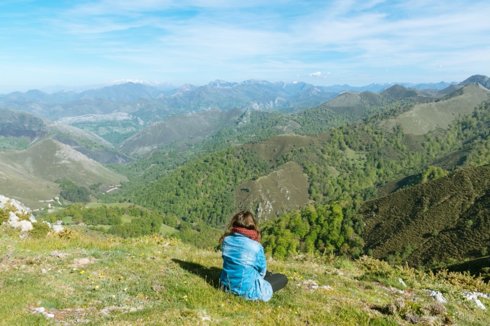 Sandra sentada de espaldas mirando a un conjunto de montañas verdes
